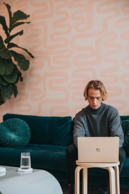 A man sitting on top of a couch using a laptop.